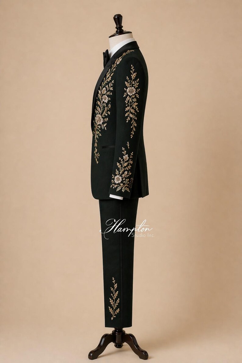 May include: A dark green suit with gold floral embroidery on the jacket and pants. The suit is displayed on a mannequin with a black bow tie and white dress shirt. The suit is a formal wear item.