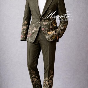 May include: Olive green suit with floral embroidery on the sleeves and pant legs. The suit includes a blazer and matching pants. The suit is displayed on a mannequin. The text "Hampton Studio Inc." is visible on the suit.
