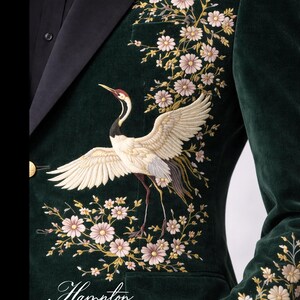 May include: Dark green velvet blazer with an embroidered crane and floral design. The crane has white wings, a black and red head, and is surrounded by pink and gold flowers. The blazer has a black lapel and a gold button.