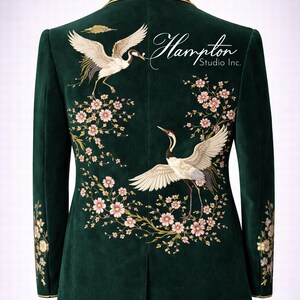 May include: Emerald green velvet blazer with embroidered crane and floral design. The back features two cranes with outstretched wings, surrounded by pink blossoms. The text "Hampton Studio Inc." is also visible.