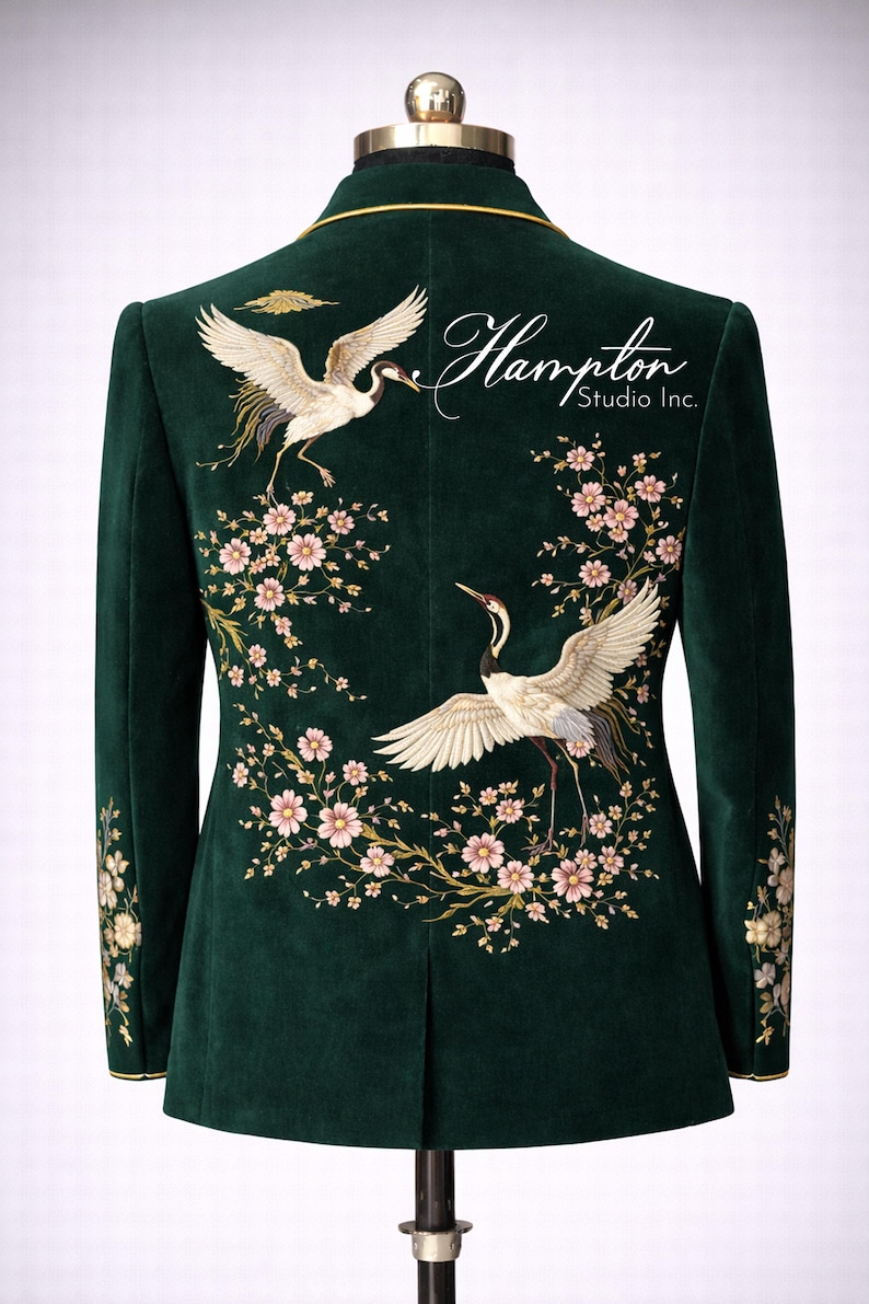 May include: Emerald green velvet blazer with embroidered crane and floral design. The back features two cranes with outstretched wings, surrounded by pink blossoms. The text "Hampton Studio Inc." is also visible.