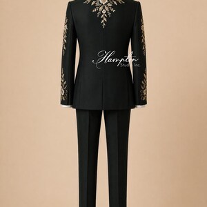 May include: A black suit with floral embroidery on the shoulders and sleeves, displayed on a mannequin. The suit includes a jacket and matching trousers. The back of the jacket features a floral design. The suit is formal wear.