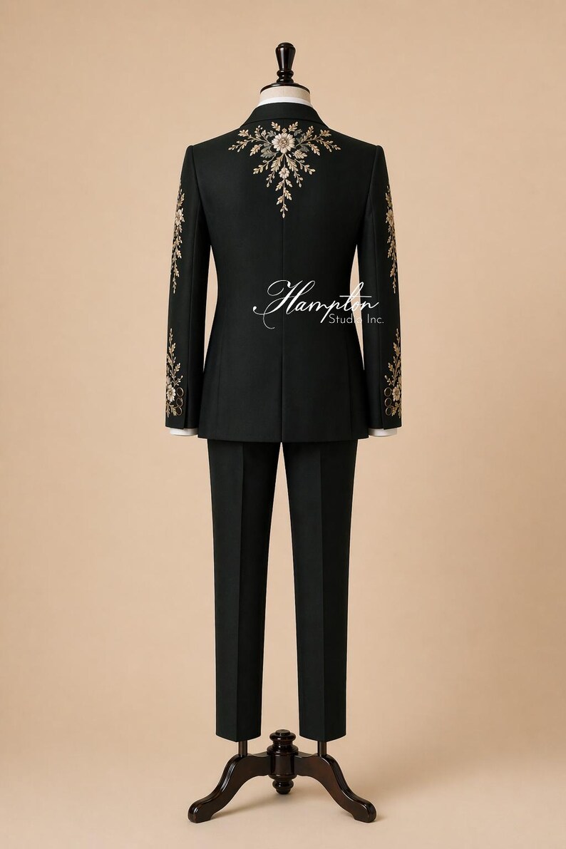 May include: A black suit with floral embroidery on the shoulders and sleeves, displayed on a mannequin. The suit includes a jacket and matching trousers. The back of the jacket features a floral design. The suit is formal wear.