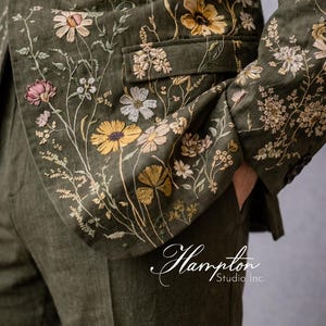 May include: Olive green blazer and pants set with intricate floral embroidery in yellow, white, and pink. The jacket features a notched lapel and a single-button closure. The text "Hampton Studio Inc." is visible.