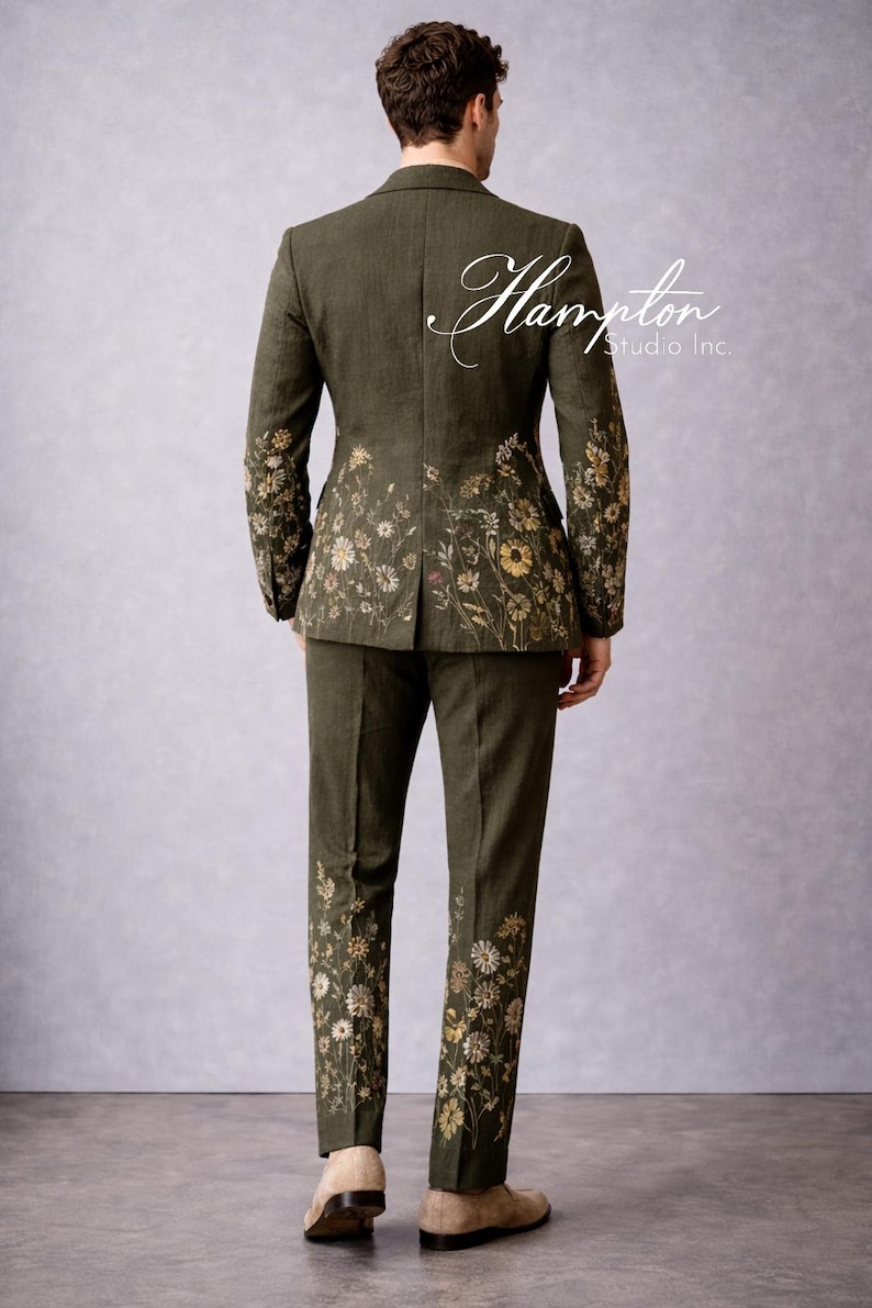 May include: Olive green suit with floral embroidery. The suit features a jacket and matching pants, both adorned with delicate flower patterns in shades of yellow and white. The text "Hampton Studio Inc." is on the back of the jacket.