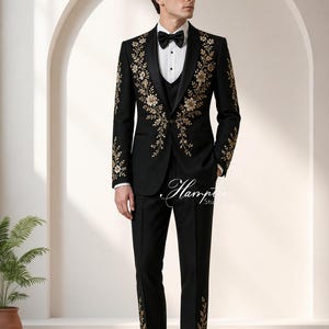 May include: Black tuxedo with gold floral embroidery. The suit includes a jacket, vest, and trousers. The jacket features ornate gold floral designs on the lapels and sleeves. The trousers have matching floral accents. A black bow tie completes the formal ensemble.