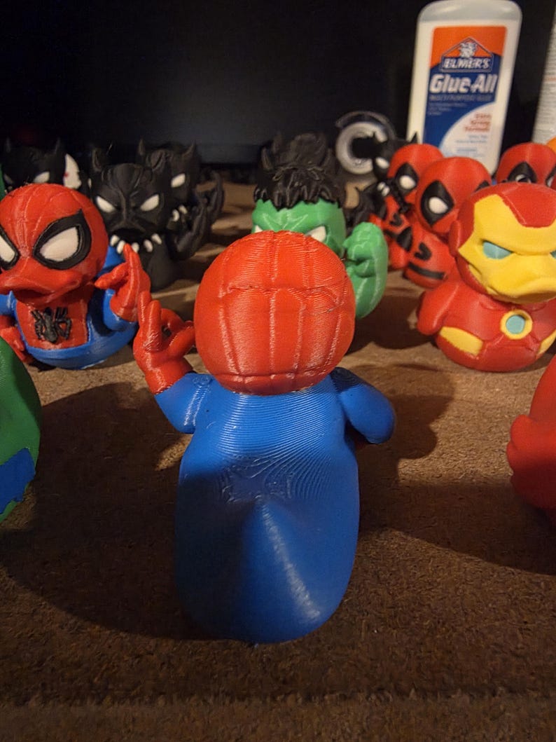 K&ouml;nnte beinhalten: Eine Sammlung von 3D-gedruckten Superheldenfiguren, darunter Spider-Man, Hulk, Iron Man und Deadpool. Die Spider-Man-Figur befindet sich im Vordergrund, mit rotem Kopf und blauem K&ouml;rper. Weitere Figuren sind in verschiedenen Farben.