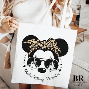 May include: White tote bag featuring a black and tan graphic of a mouse with sunglasses and a leopard print bow. The text "Making Disney Memories" is printed below the graphic. The bag has white straps.