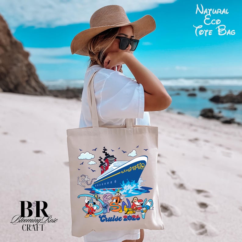 May include: A beige canvas tote bag featuring a graphic of a blue and white cruise ship on the water, surrounded by cartoon characters and the text "Disney Cruise 2026". The bag has two shoulder straps and is made of a natural, light-colored fabric.