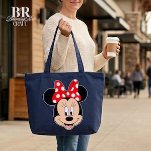 Puede incluir: Bolso tote azul marino con un dise&ntilde;o de Minnie Mouse. El bolso tiene un lazo rojo con lunares blancos y un cierre de cremallera. El bolso lo lleva una persona.