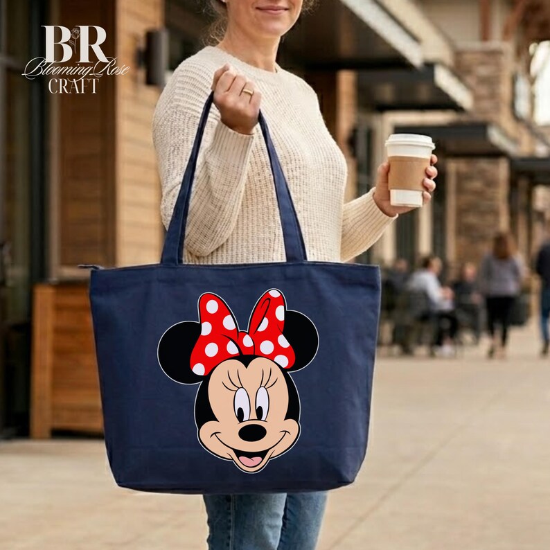 Puede incluir: Bolso tote azul marino con un dise&ntilde;o de Minnie Mouse. El bolso tiene un lazo rojo con lunares blancos y un cierre de cremallera. El bolso lo lleva una persona.