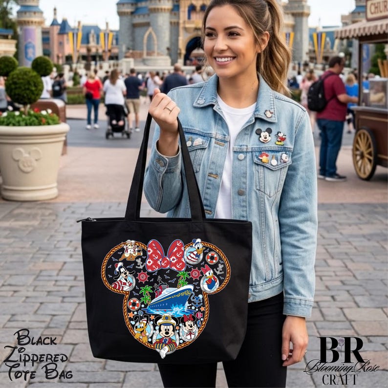 Puede incluir: Un bolso tote de lona negra con cierre de cremallera que presenta un gran gr&aacute;fico de un crucero dentro de una silueta de orejas de Mickey Mouse. El dise&ntilde;o incluye personajes de dibujos animados y un lazo rojo de lunares.