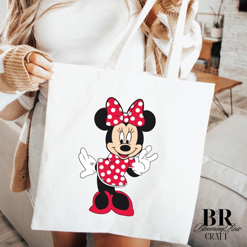 Peut inclure: Sac fourre-tout blanc avec une illustration de Minnie Mouse. Minnie Mouse porte une robe rouge &agrave; pois blancs, un n&oelig;ud assorti et des oreilles noires. Le sac a des anses blanches et le texte "BR Blooming Rose Craft".