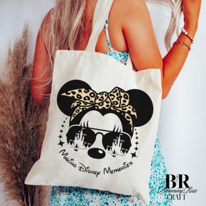 May include: Cream-colored tote bag featuring a black Minnie Mouse design with sunglasses and a leopard print bow. The text "Making Disney Memories" is printed below the graphic. The bag has two handles.