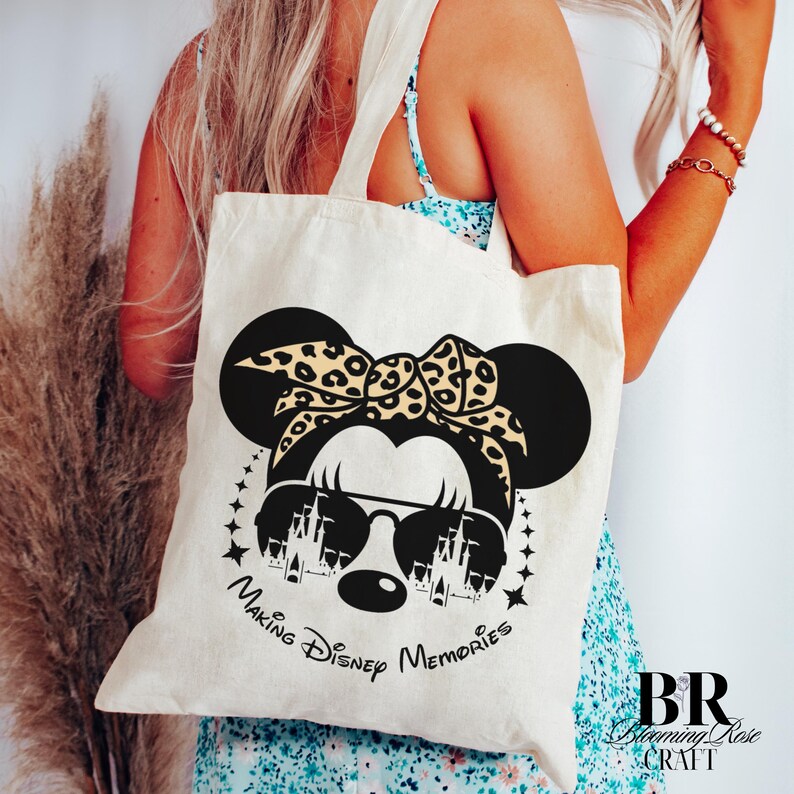 May include: Cream-colored tote bag featuring a black Minnie Mouse design with sunglasses and a leopard print bow. The text "Making Disney Memories" is printed below the graphic. The bag has two handles.