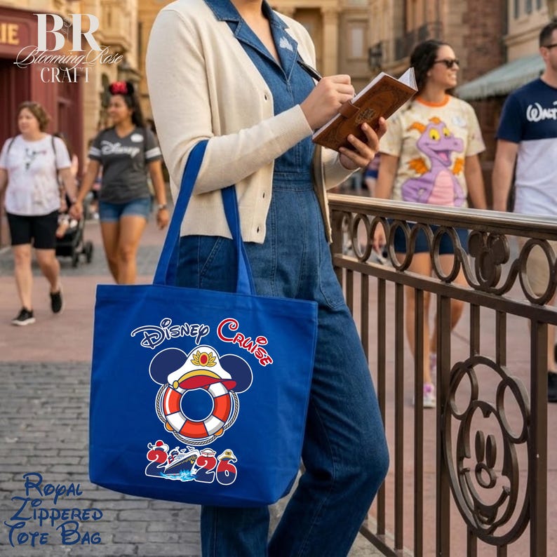 Puede incluir: Un bolso tote azul real con un gr&aacute;fico de un salvavidas con orejas de Mickey Mouse y una gorra de capit&aacute;n. El texto dice Disney Cruise 2026. El dise&ntilde;o incluye una peque&ntilde;a ilustraci&oacute;n de un crucero sobre el a&ntilde;o 2026 en la parte inferior.