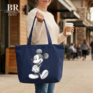 May include: Navy blue tote bag featuring a smiling Mickey Mouse graphic. The bag has a zipper closure and long handles. The Blooming Rose Craft logo is in the upper left corner. The bag is carried by a person.