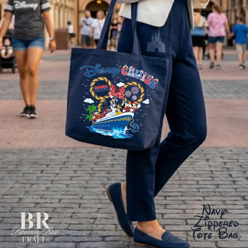 May include: A navy blue tote bag featuring a graphic of a cruise ship with Disney characters, including Mickey and Minnie Mouse. The design includes the text Disney Cruise 2026, palm trees, and rope accents. The bag has two shoulder straps.
