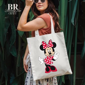 Peut inclure: Sac fourre-tout cr&egrave;me avec un motif de Minnie Mouse. Le personnage de dessin anim&eacute; porte une robe et un n&oelig;ud &agrave; pois rouges, avec des oreilles et des chaussures noires. Le sac porte le texte "BR Blooming Rose Craft" en haut &agrave; gauche.