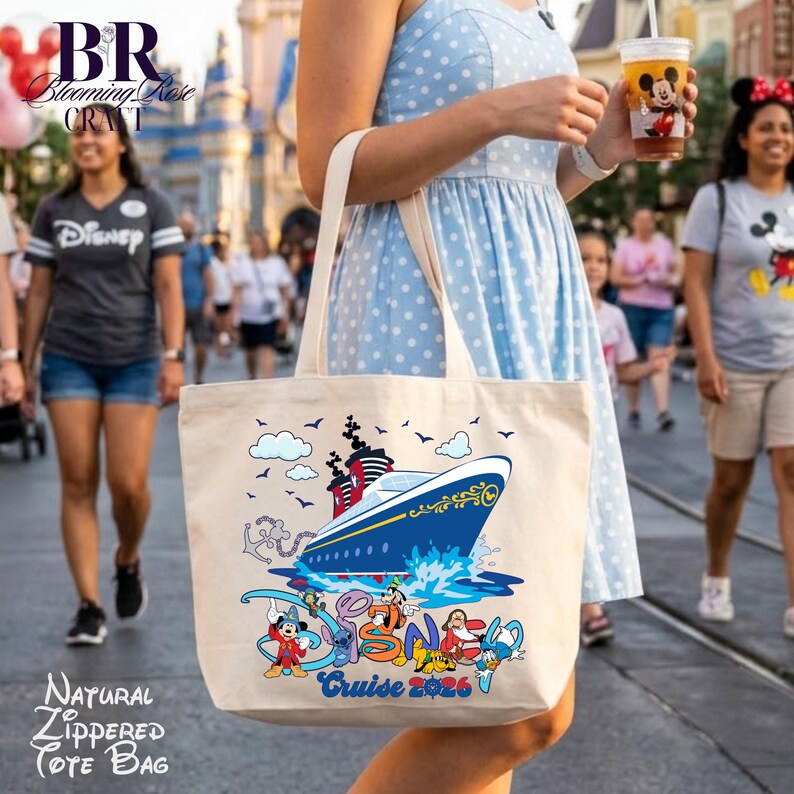 May include: A natural-colored canvas tote bag featuring a graphic of a blue and white cruise ship sailing on water. Below the ship, colorful cartoon characters are depicted alongside the text Cruise 2026. The bag has two shoulder straps.