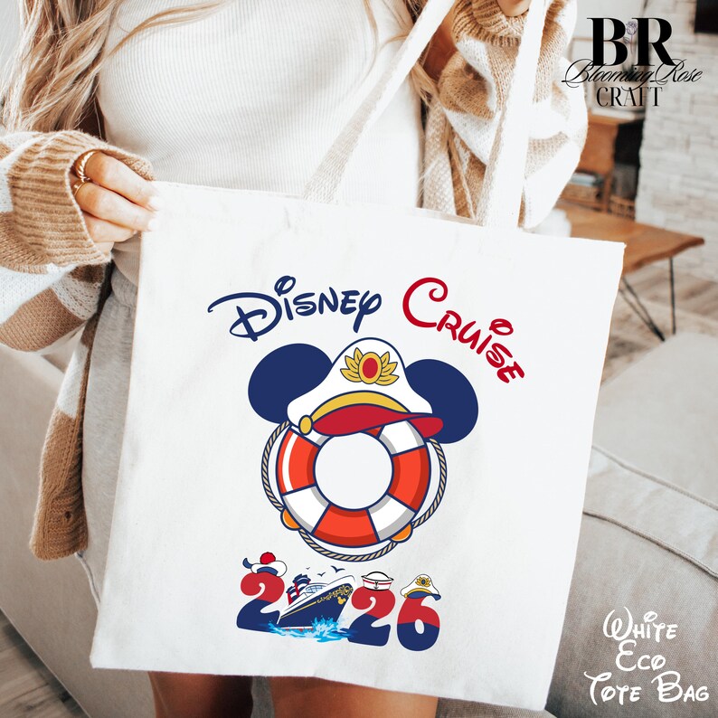 Puede incluir: Una bolsa de tela blanca con un gr&aacute;fico de un salvavidas con orejas de Mickey Mouse y una gorra de capit&aacute;n. Debajo, el texto 2026 incorpora un crucero y gorros n&aacute;uticos. Las palabras Disney Cruise est&aacute;n impresas en azul y rojo sobre el gr&aacute;fico.