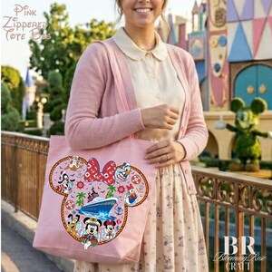 Puede incluir: Un bolso tote de color rosa claro con cremallera que presenta un gran gr&aacute;fico con la silueta de Mickey Mouse, relleno de personajes Disney de tem&aacute;tica n&aacute;utica como Mickey, Minnie, Donald, Goofy y Pluto, junto a un crucero y anclas.