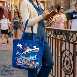 May include: A bright blue tote bag featuring a graphic of a cruise ship sailing on water, with an anchor and various cartoon characters below. The text "Cruise 2026" is printed in colorful letters at the bottom of the bag, which is held by a person.