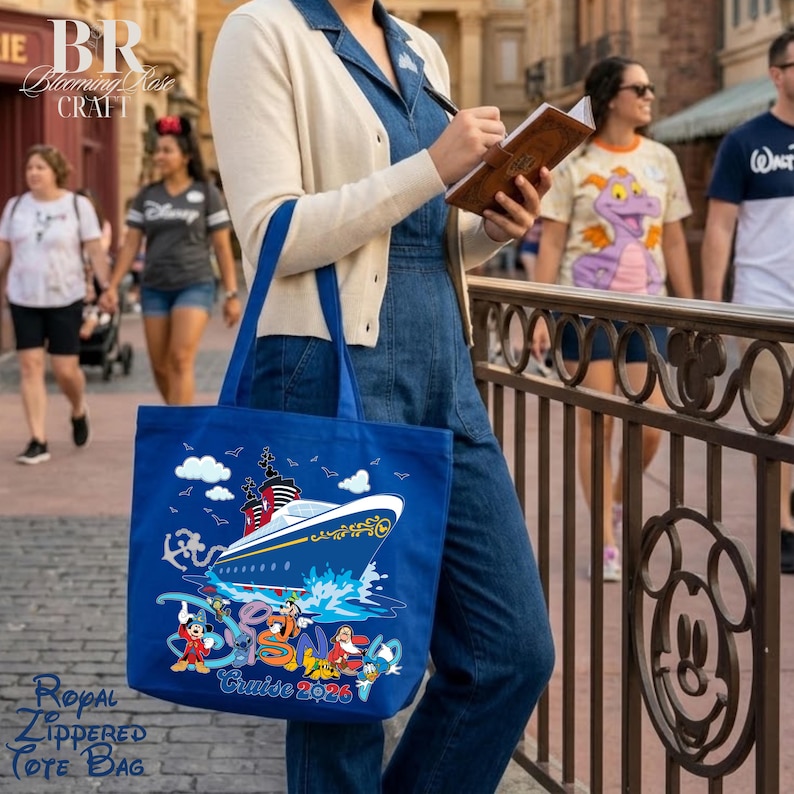May include: A bright blue tote bag featuring a graphic of a cruise ship sailing on water, with an anchor and various cartoon characters below. The text "Cruise 2026" is printed in colorful letters at the bottom of the bag, which is held by a person.