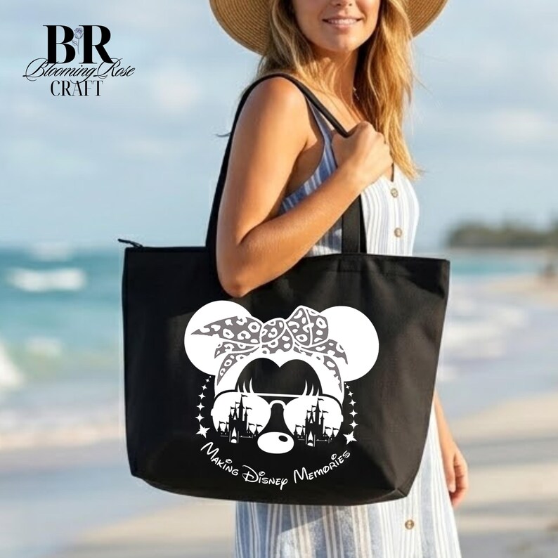 May include: Black tote bag featuring a white Minnie Mouse design with sunglasses and a bow. The bag has the text "Making Disney Memories" and is carried by a person on a beach.
