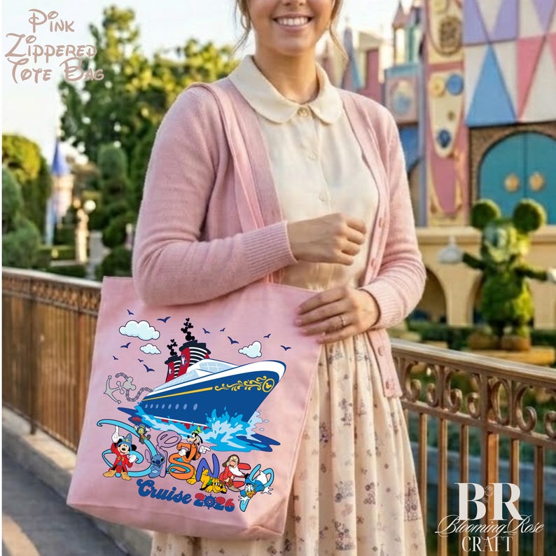 May include: A light pink tote bag featuring a graphic of a cruise ship sailing on blue water. The design includes Disney characters such as Mickey Mouse, Stitch, and Goofy, with the text "Cruise 2026" printed in blue at the bottom of the bag.