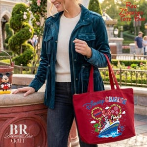 May include: A red zippered tote bag featuring a graphic of a cruise ship with Mickey and Minnie Mouse, the text Disney Cruise, and the year 2026. The bag has two red shoulder straps and a zipper closure along the top edge for secure storage.