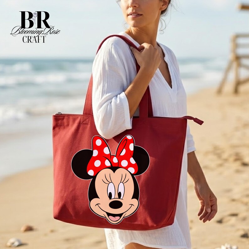 Puede incluir: Un bolso tote rojo con un dise&ntilde;o de Minnie Mouse, con un lazo de lunares blancos. El bolso tiene cierre de cremallera y lo lleva una persona en la playa. El logotipo de Blooming Rose Craft est&aacute; en la esquina superior izquierda.