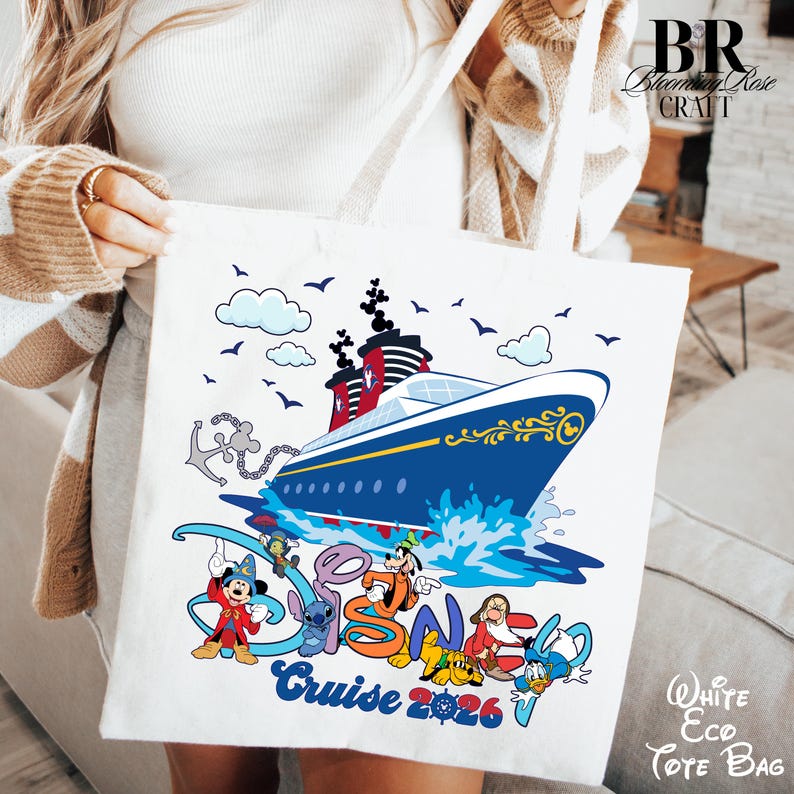 May include: A white tote bag featuring a colorful graphic of a cruise ship on the water with an anchor and various cartoon characters. The text reads "Disney Cruise 2026" in blue and orange lettering, accompanied by small clouds and birds in the sky.