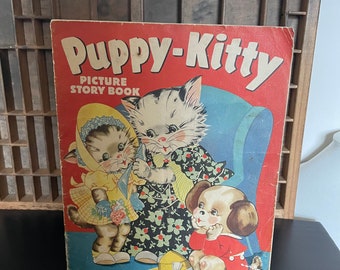 May include: A vintage children's picture story book titled "Puppy-Kitty" featuring illustrations of a cat, a kitten, and a puppy wearing clothes. The book cover is red with white lettering and has a blue and white armchair in the background.