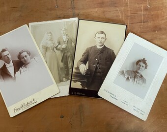 May include: Four vintage black and white photographs of people. The photos are arranged in a staggered pattern on a wooden surface. The photos are all in portrait orientation and feature people in formal attire. The photos are all from different photographers and have different borders and text.