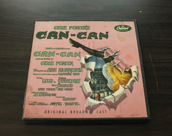 May include: A pink and green record album cover for the musical "Can-Can" by Cole Porter. The cover features a woman in a red dress and black stockings kicking her leg up in the air. The text on the cover reads "Cole Porter's Can-Can" and "Original Broadway Cast".