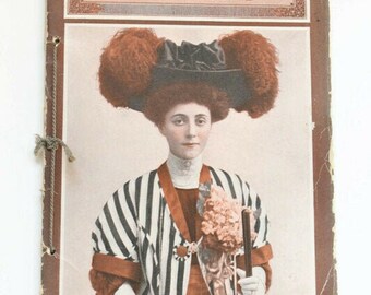 May include: The cover of a vintage magazine, "The Burr McIntosh Monthly", from July 1908. The cover features a woman in a black and white striped jacket, a large hat with red feathers, and a bouquet of flowers.