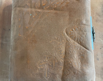 May include: A vintage brown photo album with a worn canvas cover and embossed floral designs. The album has a metal clasp and the words "Our Home" are embossed on the front.