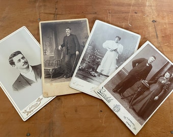 May include: Four vintage black and white photographs of people. The photos are arranged in a stack on a wooden surface. The photos are all in portrait orientation and feature people in formal attire.