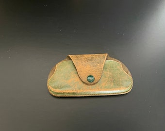 May include: A green and brown leather glasses case with a green button closure.