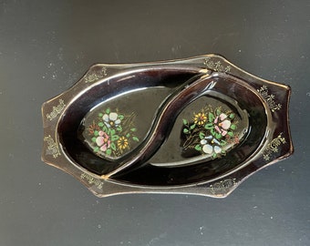 May include: A black ceramic serving dish with two divided sections. The dish is decorated with gold trim and hand-painted floral designs in shades of pink, white, and yellow.