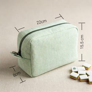 May include: A rectangular, light green striped cosmetic bag with a black zipper, measuring approximately 8cm x 22cm x 15.5cm. The bag is next to several Mahjong tiles. The bag is designed for storing makeup and other beauty products.