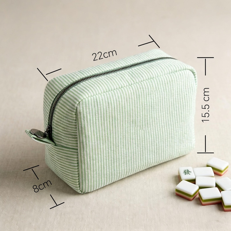 May include: A rectangular, light green striped cosmetic bag with a black zipper, measuring approximately 8cm x 22cm x 15.5cm. The bag is next to several Mahjong tiles. The bag is designed for storing makeup and other beauty products.