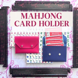 May include: A Mahjong card holder with the text "MAHJONG CARD HOLDER" in a pink font. The image shows a pink and a blue card holder, each with a snap closure. The background includes Mahjong tiles and a floral pattern.