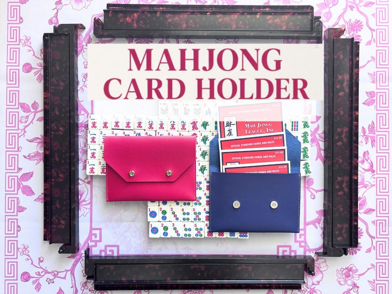 May include: A Mahjong card holder with the text "MAHJONG CARD HOLDER" in a pink font. The image shows a pink and a blue card holder, each with a snap closure. The background includes Mahjong tiles and a floral pattern.