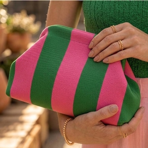 Pode incluir: Uma bolsa clutch com um padr&atilde;o de riscas verticais arrojado, alternando entre as cores rosa vibrante e verde floresta. A bolsa tem um design estruturado com uma arma&ccedil;&atilde;o superior arredondada, exterior em tecido texturizado e silhueta suave.
