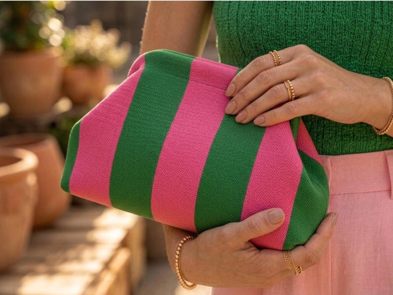 Pode incluir: Uma bolsa clutch com um padr&atilde;o de riscas verticais arrojado, alternando entre as cores rosa vibrante e verde floresta. A bolsa tem um design estruturado com uma arma&ccedil;&atilde;o superior arredondada, exterior em tecido texturizado e silhueta suave.