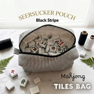 May include: A black and white striped seersucker pouch labeled "SEERSUCKER POUCH Black Stripe" filled with white Mahjong tiles. The text "Mahjong TILES BAG" is below the pouch. The pouch is open, revealing the tiles inside.