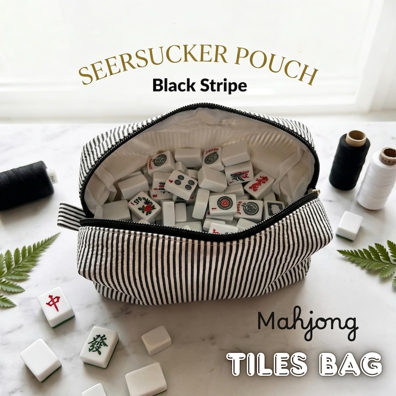 May include: A black and white striped seersucker pouch labeled "SEERSUCKER POUCH Black Stripe" filled with white Mahjong tiles. The text "Mahjong TILES BAG" is below the pouch. The pouch is open, revealing the tiles inside.
