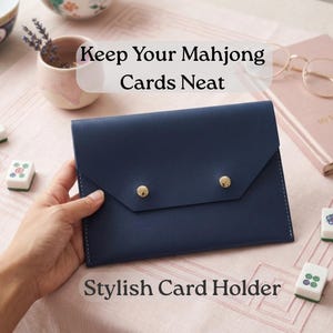 May include: A navy blue card holder with gold button closures. The text "Keep Your Mahjong Cards Neat" and "Stylish Card Holder" are visible. Mahjong tiles and a pink journal are also present.